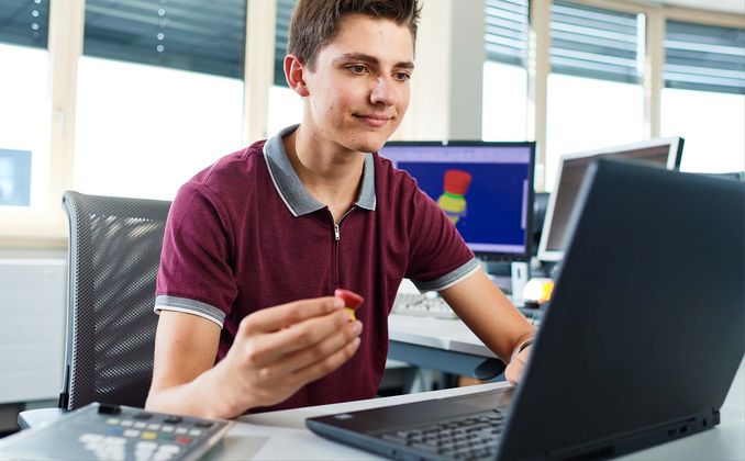 Ein Student im Bereich Konstruktion und Entwicklung sitz an seinem Arbeitsplatz in der Konstruktion und betrachtet eine Not-Halt-Konstruktion.